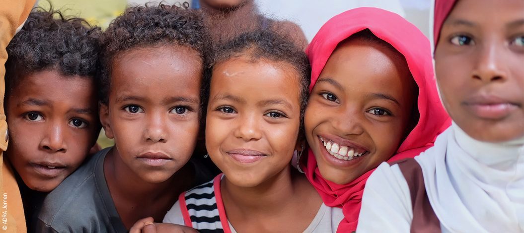 fünf Kinder aus dem Jemen blicken in die Kamera – einige ernst, andere lächelnd, eines trägt ein rotes Kopftuch | © ADRA Jemen