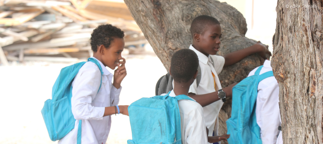 Header_Somalia_PRO-7160086©-pxsfylqaiwcd0hq59dbpxtt5zibbtmc6625v1kq90c Vier junge Schüler in Somalia mit ihren hellblauen Rucksäcken, sind auf dem Weg zur Schule.